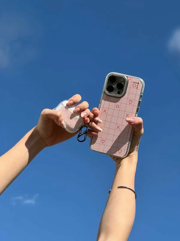 Two hands holding up pink grid cases against a blue sky